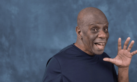 Jimmie "JJ" Walker smiles in front of a blue backdrop.