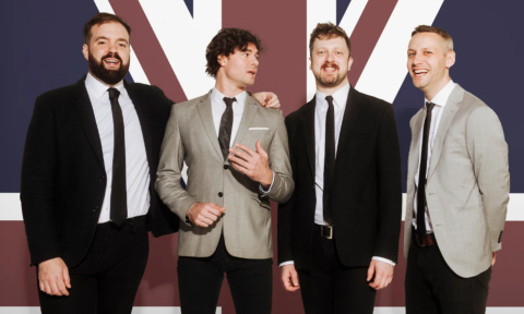 Bandmates from the Brit Pack smile and pose in front of the British flag.