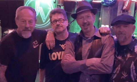 Bandmates from The Nighthawks smile and pose in front of a green backdrop.