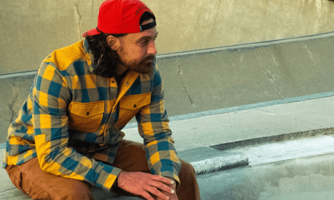 Will Evans, dressed in a bright red cap and plaid shirt, poses casually on a bench.