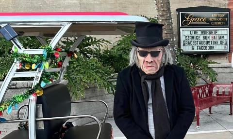 A character representing Ebenezer Scrooge stands next to a tour EV