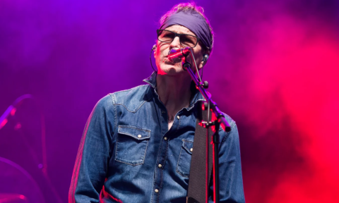 The lead vocalist for BoDeans performs on stage in front of a purple and pink backdrop.