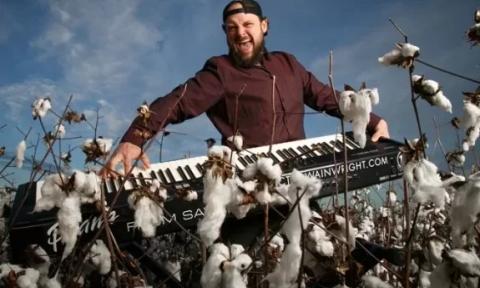 Victor Wainwright smiles and plays the keyboard in front of a blue backdrop.