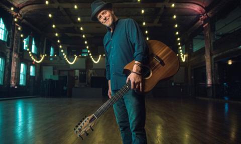 Willy Porter smiles while posing with his guitar.
