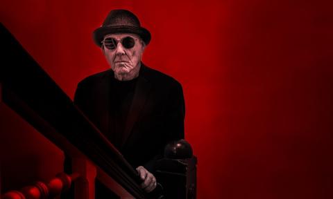 Billy Price poses with black clothing and matching shades in front of a red backdrop.