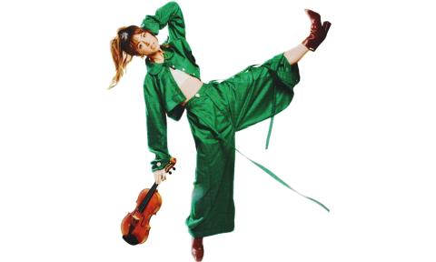 Lindsey Stirling wears a green outfit and poses with her violin.