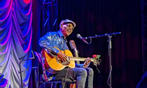 Guy Davis, with his guitar on a stage draped in blue light