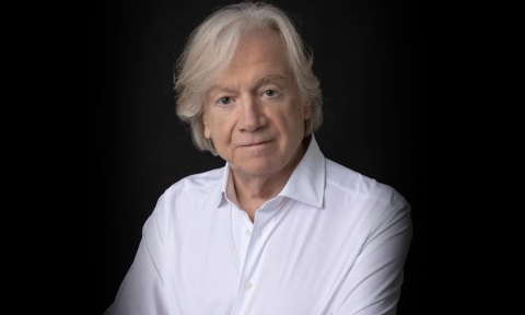 Justin Hayward wears a white shirt and poses in front of a black backdrop.