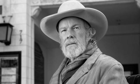 Robert Earl Keen sports a cowboy hat as he poses for a striking black-and-white portrait.