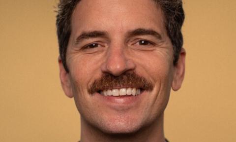 Zane Helberg smiles and poses in front of a mustard colored backdrop.