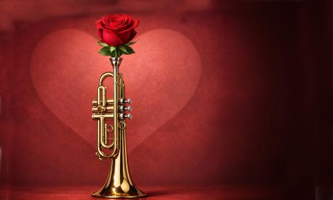 A red rose in the mouthpiece of a trumpet standing against a red heart