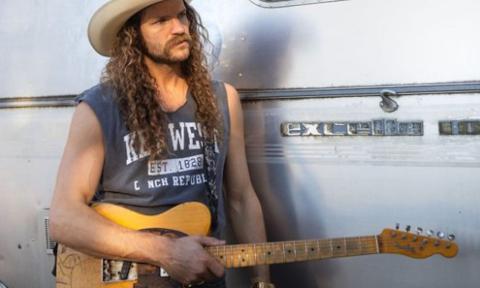 Andy Thomas wears a cowboy hat and poses with his guitar.