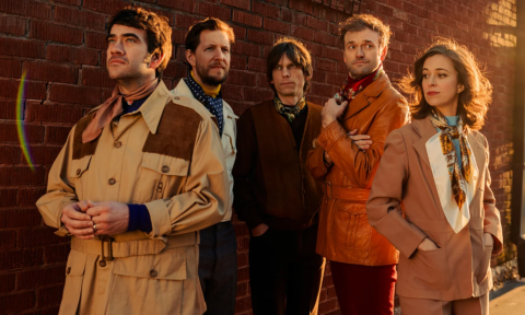 Bandmates from the Punch Brothers wear coats and pose in front of a wall.
