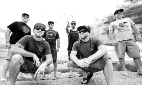Bandmates from Slightly Stoopid pose on rocks in front of an ocean.