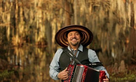 Terrance Simien beams as he stands before a scenic bayou backdrop.