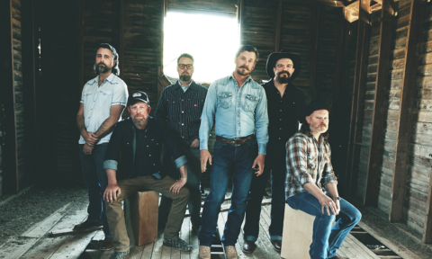 Bandmates from Turnpike Troubadours pose in a room with exposed wood on the walls and floor.