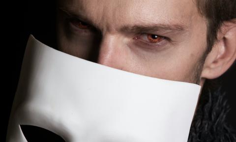 A vampire removes his mask, revealing his blood red eyes.