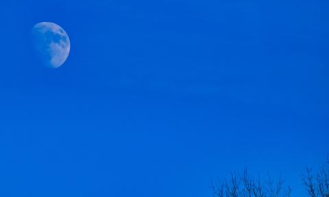 A nearly full moon in a dark blue sky
