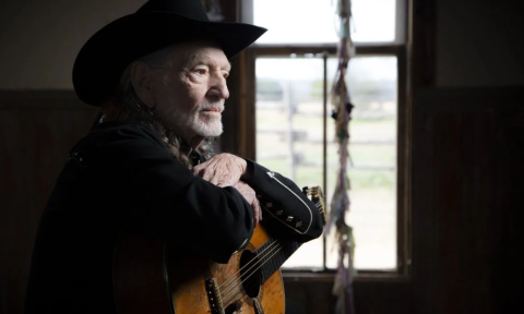 Willie Nelson grips his guitar, gazing ahead in quiet reflection.