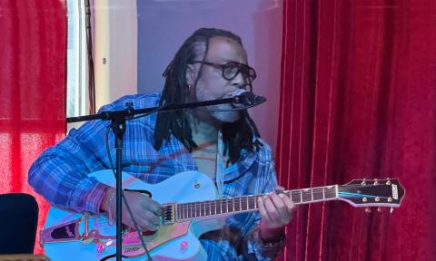 Guitarist Erick Carter, in blue, performing in front of a red curtain