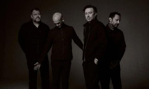 Bandmates from Rise Against wear dark clothing and pose in front of a black backdrop.