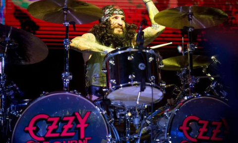 A bandmate from Tommy's Rocktrip smiles and performs on stage.