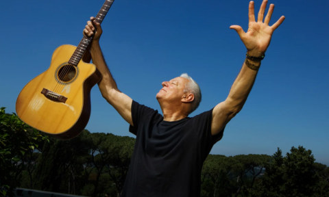 Tommy Emmanuel shuts his eyes and holds his guitar in the air.