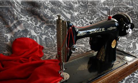 An antique Singer Sewing Maching with a black and white cloth background and red fabric under the needle