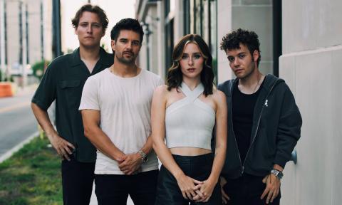 Members of First To Eleven, dressed in black and white, strike a pose on a city street.