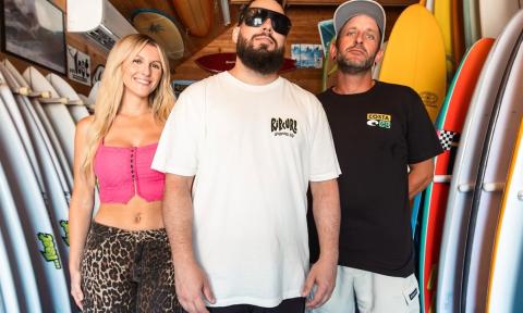 Bandmates from Seranation smile and pose next to surfboards.