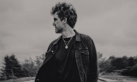 Tyler Hilton wears dark clothing and gazes at an object in the distance.