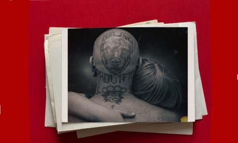 A male with a large tattoo on his head, facing backwards and hugging a blond woman