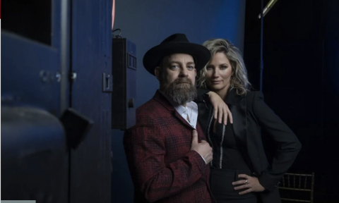 Bandmates from Sugarland huddle together and pose in front of a dark blue backdrop.