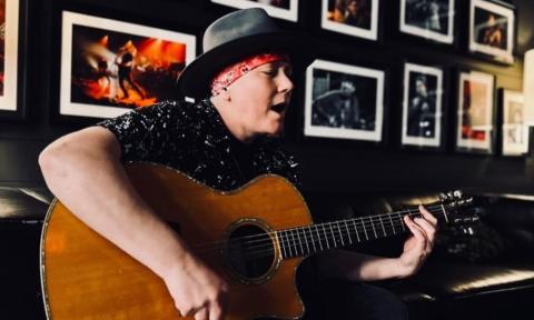 With a radiant smile, Kristy Lee strums her guitar against a backdrop of framed photographs.