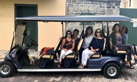 Gold Tours with their green large EV, on a St. Augustine Street with clients aboard