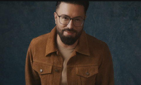 Danny Gokey dons glasses and a brown shirt in front of a grey backdrop.