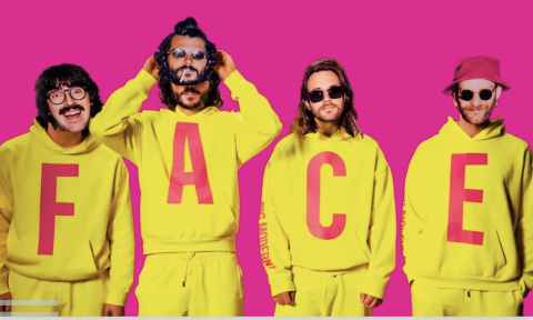 Bandmates from Goose wear yellow clothing and pose in front of a pink backdrop.