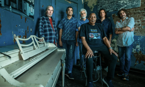 Little Feat huddle together and pose in front of a dark blue backdrop.