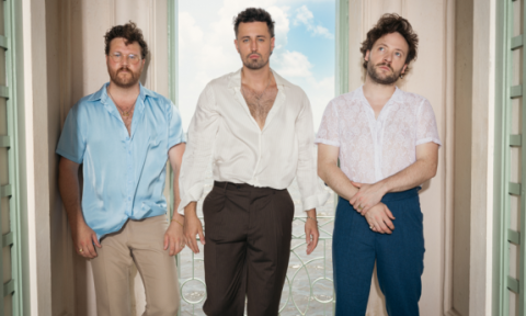 Bandmates from Raynes pose in front of a window with curtains.