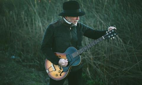 Roy Rogers wears dark formal clothing and poses with his guitar.