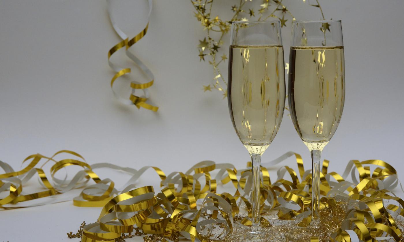 Two tall champagne flutes, full, on a white background with gold ribbon