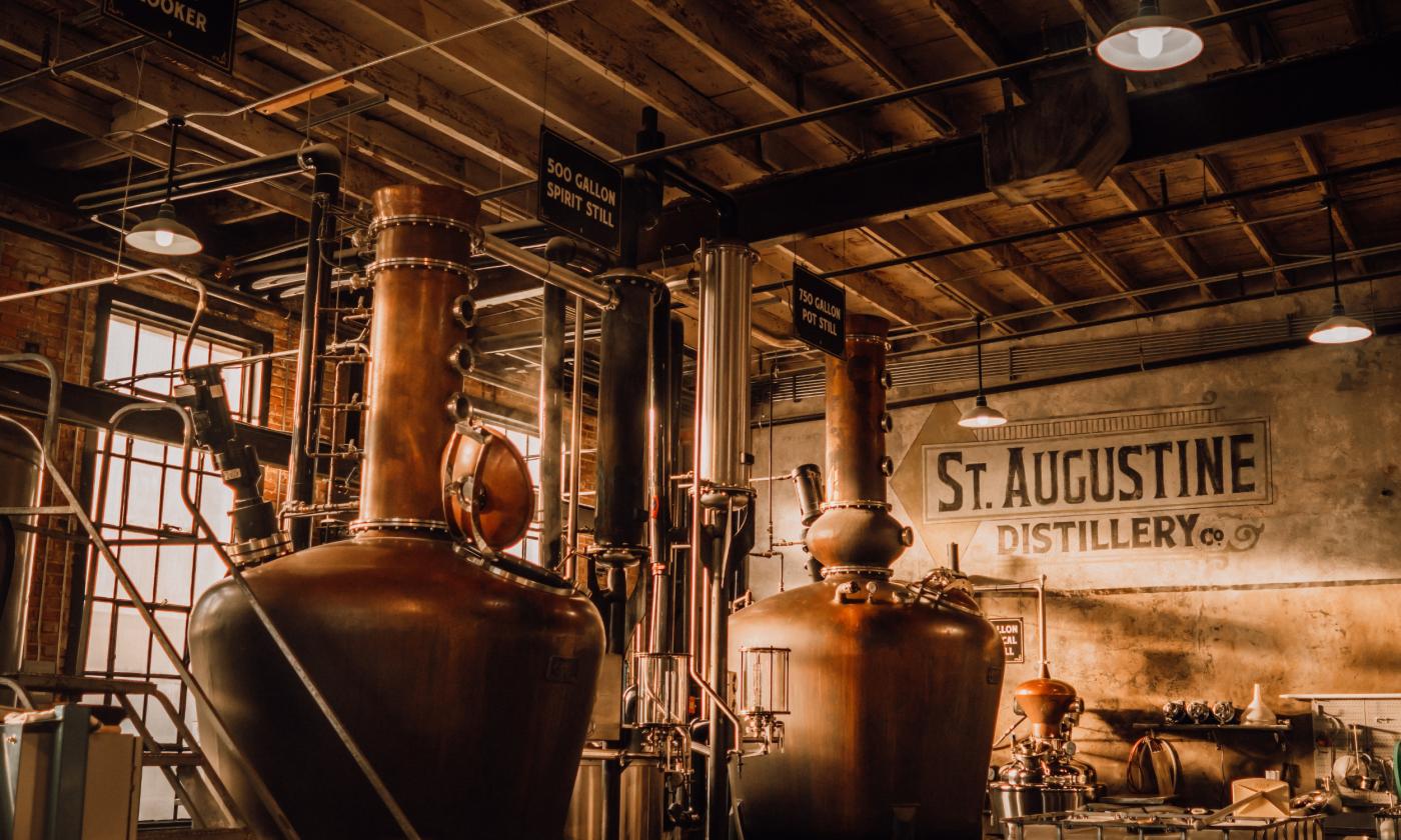The interior of St. Augustine Distillery, in sepia tones, with light shining through a large window and showing the 500-gallon containers for brewing 
