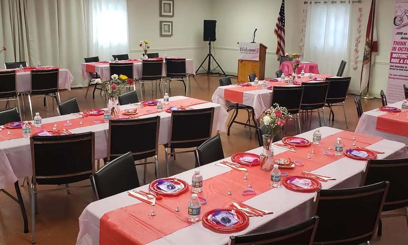 A banquet room in a small club, set up with rectangular tables for six, decorate with red runners and flowers