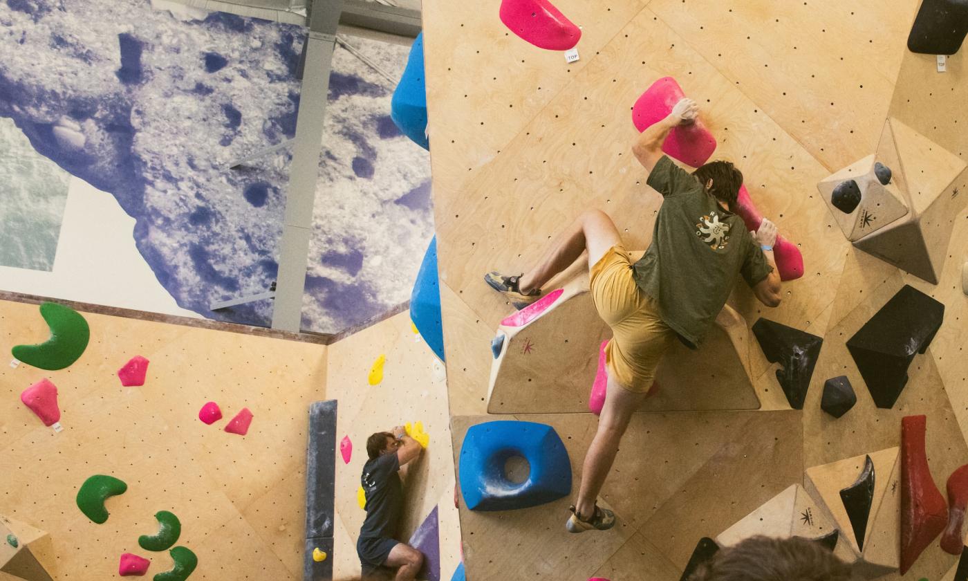 An indoor climbing wall with wooden obstacles and steps of various colors and a climber negotiating the wall