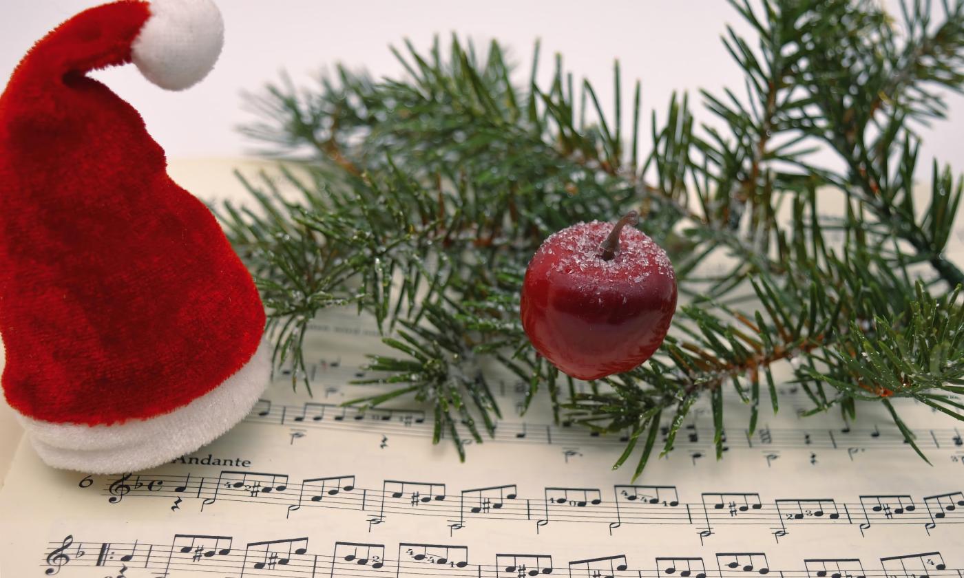 An arranged photo to show holiday music, a musical score is topped with a Santa hat, greenery, and a red apple