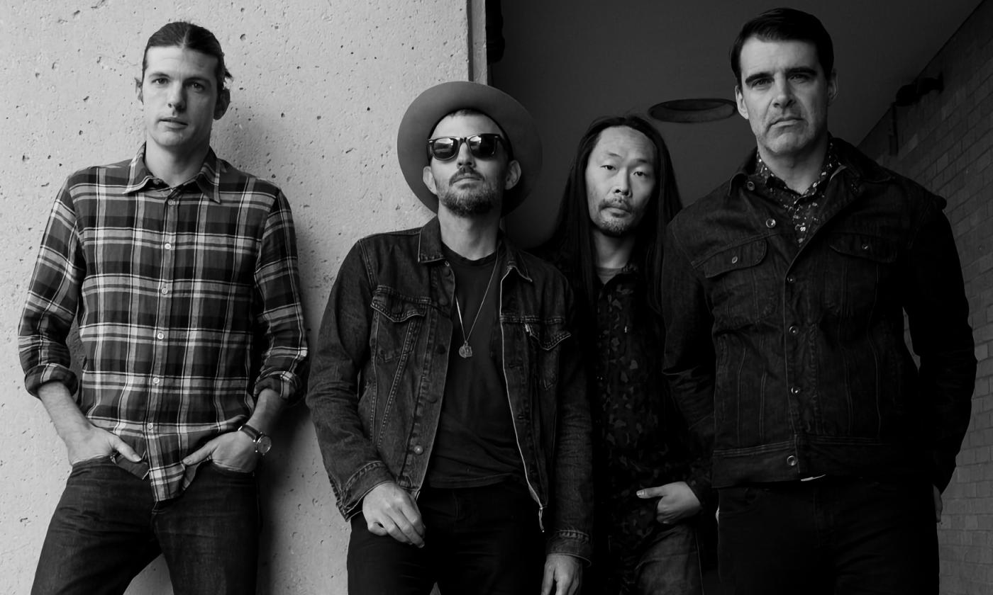 Four band members standing against a wall in a black and white photo