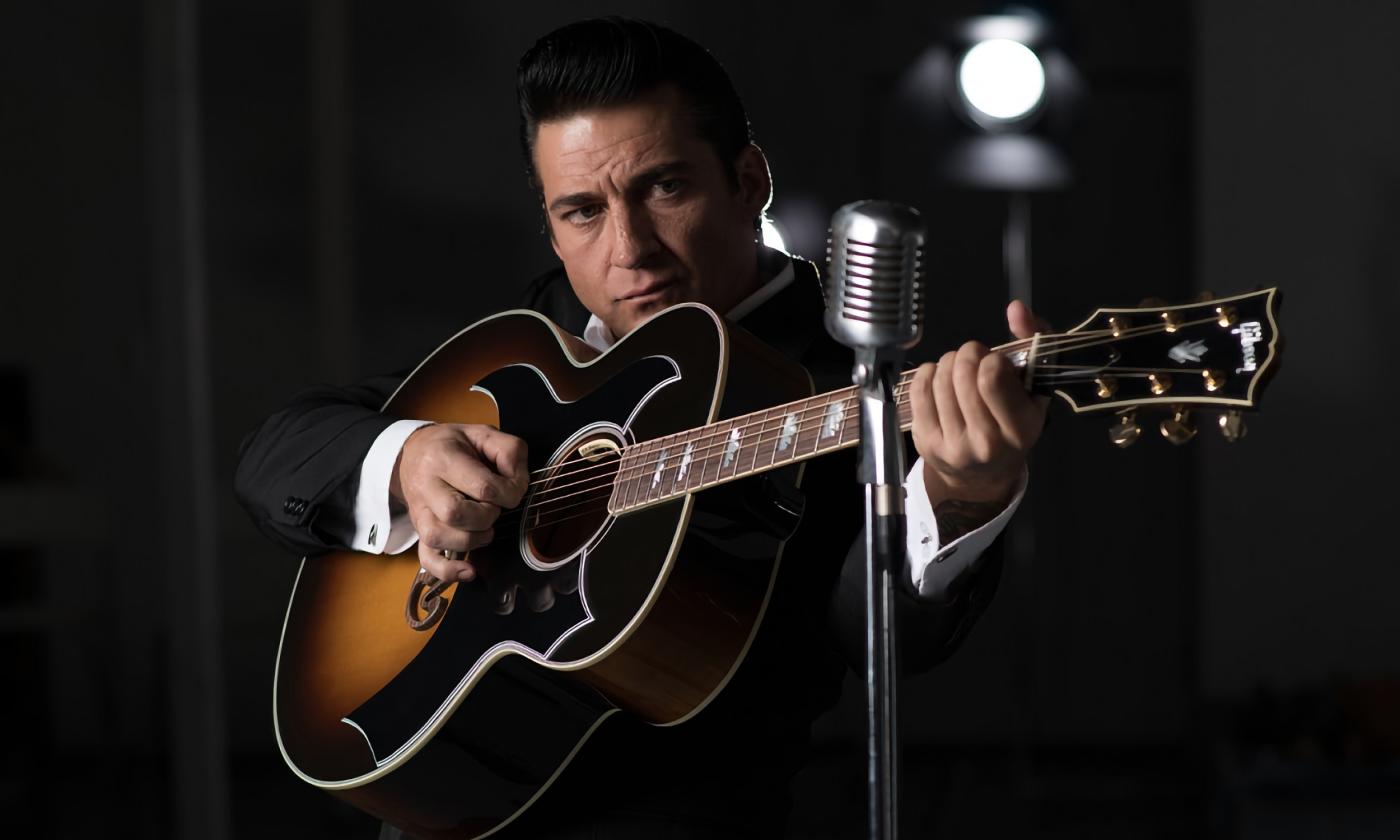 Shawn Barker, a Johnny Cash impersonator, standing with a guitar on a darkened stage