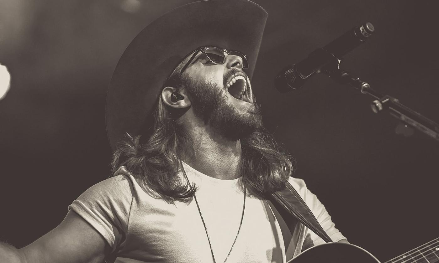 Warren Zeiders singing on a microphone with his guitar in hand. 