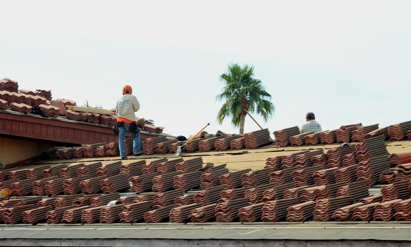Two roofers working with tile with a palm tree in the background