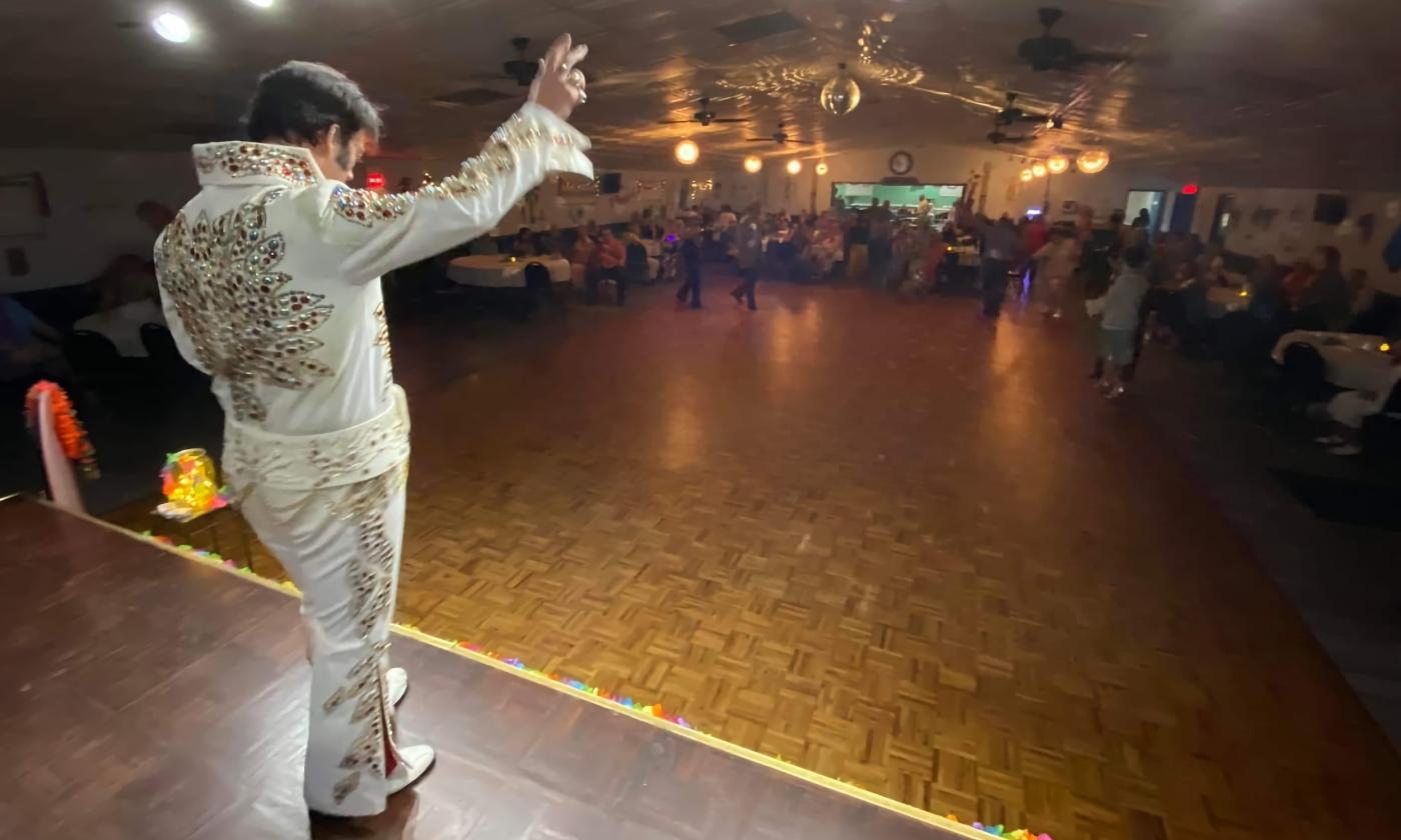 An Elvis impersonator seen from the stage performing at a dinner show